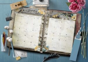 Flatlay mockup of printable 2027 A5 monthly planner inserts with vintage floral design in a ring binder on a blue desk with flowers and stationery.