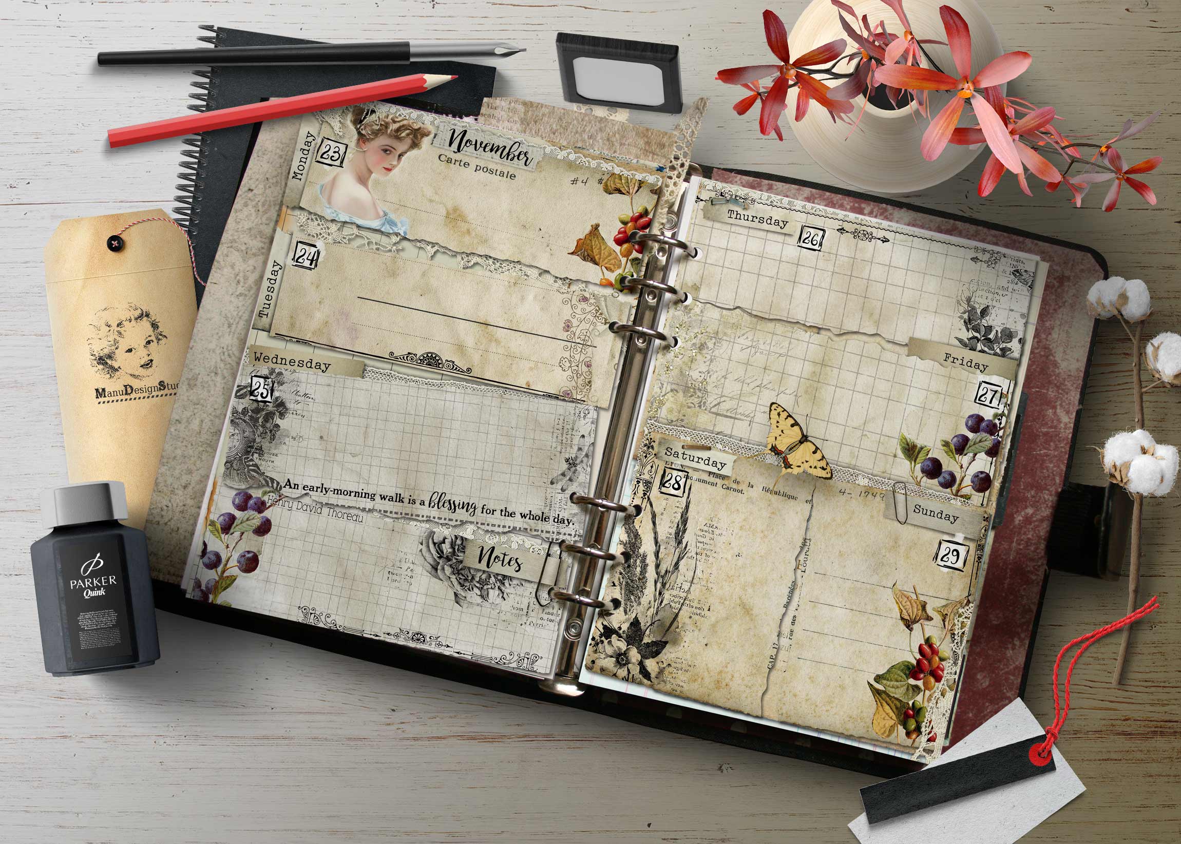 Open decorative planner on a wooden desk, filled with vintage-style pages, botanical motifs, and calendar dates, with pens and pink flowers nearby.
