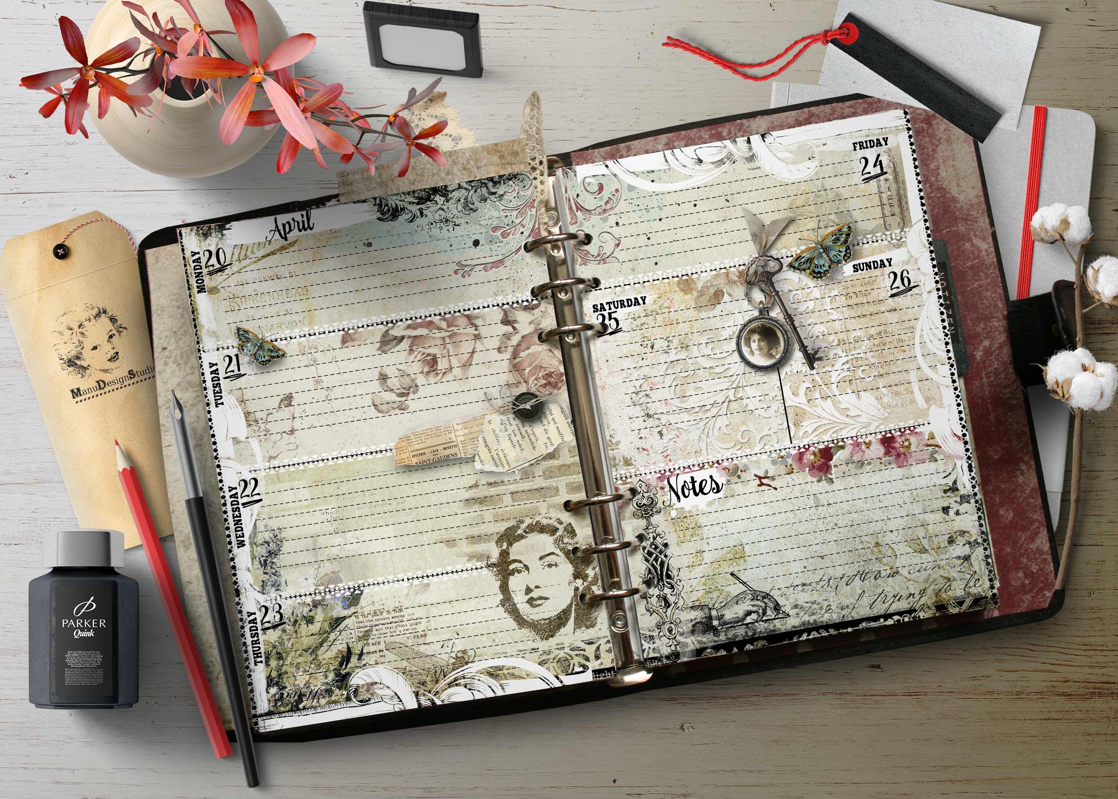 Open decorative planner on a wooden desk with a vase of pink flowers and assorted stationery nearby.