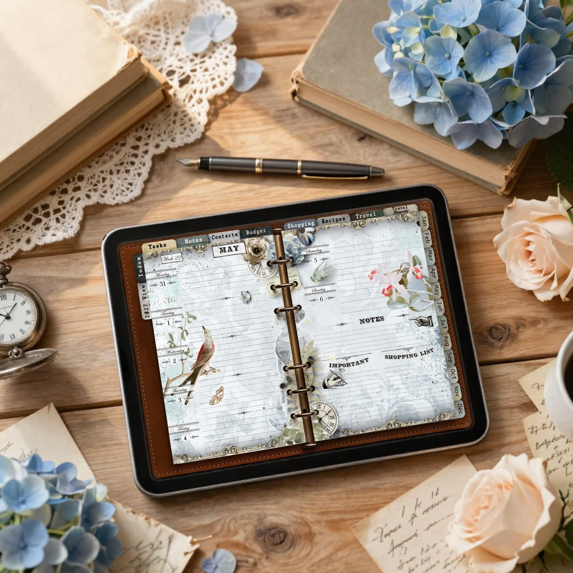 Tablet showing a decorative calendar planner on a wooden desk, with a fountain pen, lace, and blue hydrangeas nearby.