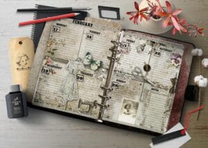 Open ring-bound planner spread with vintage calendar pages and floral embellishments on a wooden desk, surrounded by art supplies and tags.
