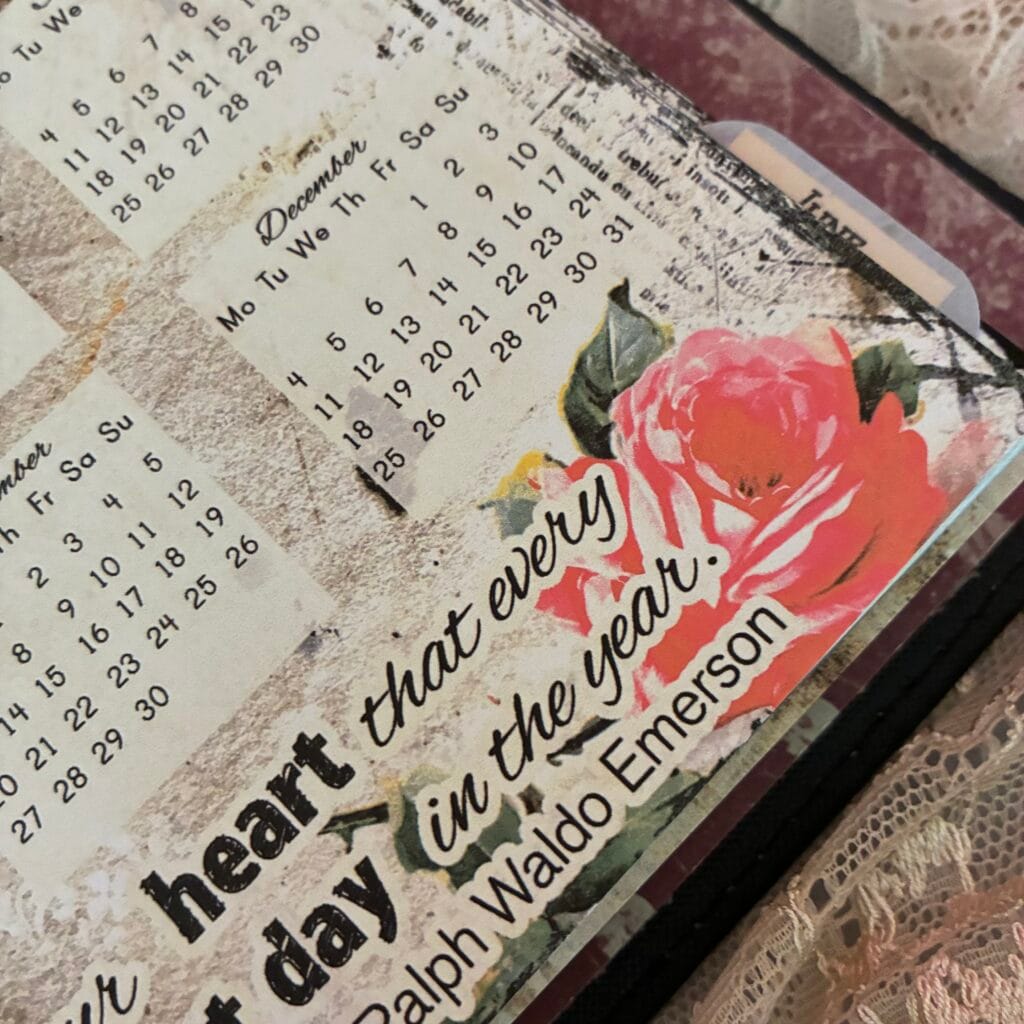 2028 Year at a Glance planner page displayed in a vintage black 6-ring planner. The page features all twelve months of 2028 in a classic calendar overview, surrounded by vintage collage elements, botanical details, handwritten textures and a decorative Ralph Waldo Emerson quote. The vintage planner is photographed on an antique lace-covered desk, creating a nostalgic and timeless atmosphere. Printable yearly calendar page available in multiple planner sizes.